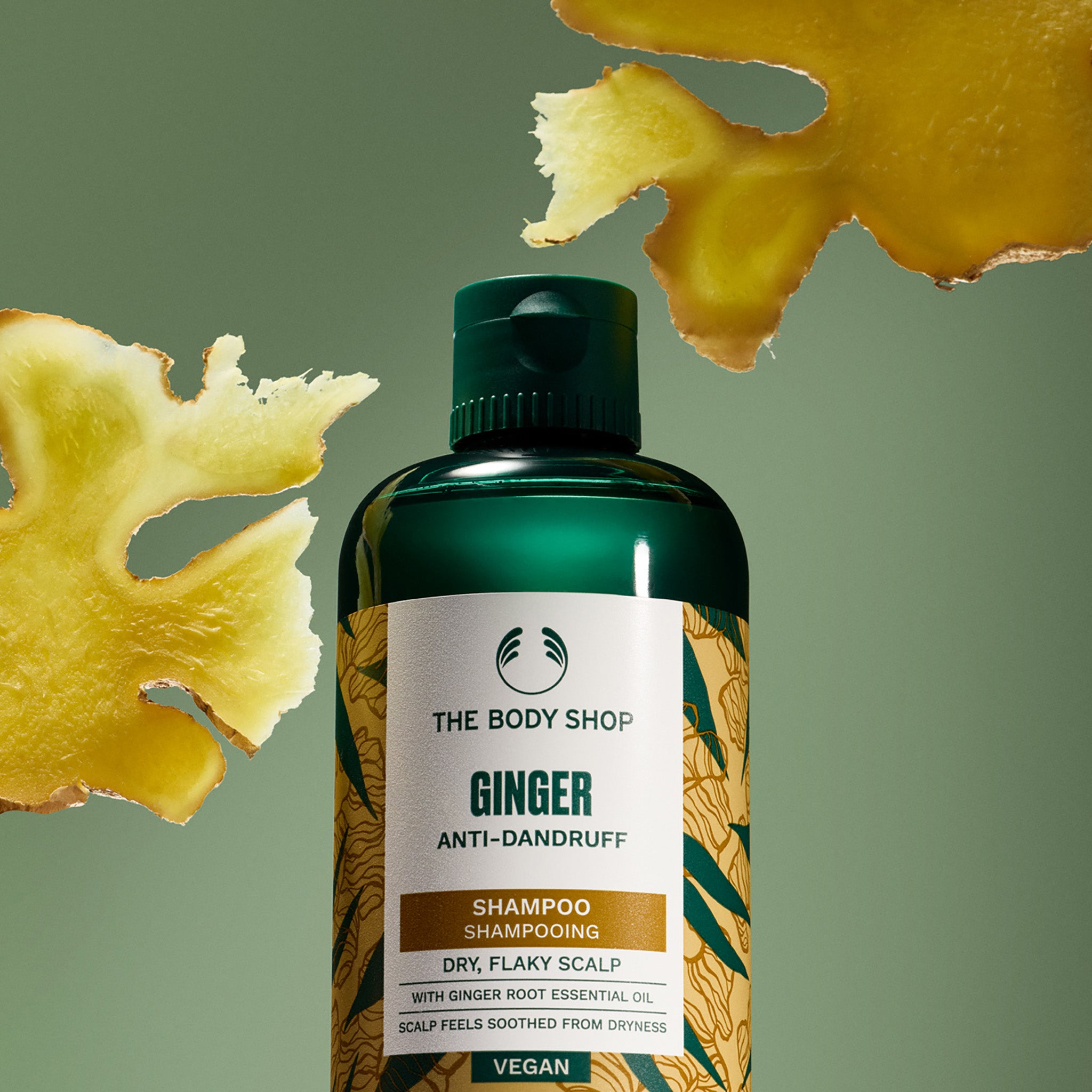 The Body Shop Ginger Anti-Dandruff Shampoo bottle with ginger root on a green background